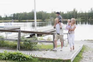 4 henkinen perhe kävelemässä Köpmanholmenin laituria pitkin auringon paisteessa. PIenet lapset ovat vanhempien sylissä, toinen heistä olkapäiden päällä istumassa.