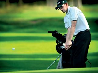 Valkopaitainen mies golfaamassa vihreällä kentällä