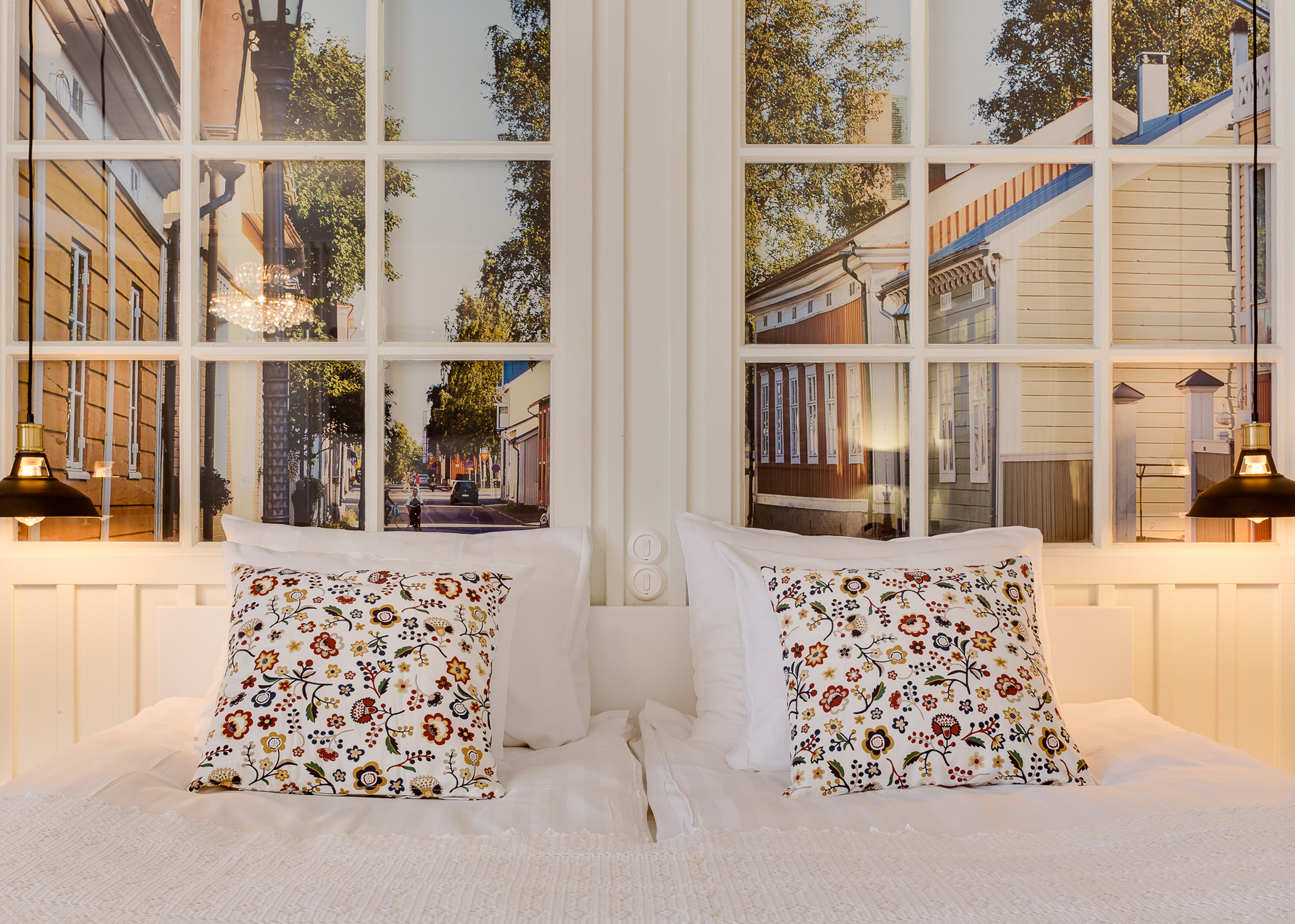 Original Sokos Hotel Kaarlen kahden hengen huoneen parivuode, jonka taustalla sängyn päätynä valkoiset ikkunakehykset joiden takana näkyy vsuuri valokuva suurennos vanhakaupunki Neristanista