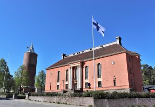 Kokkolan kaupunginteatterin rakennus Vartiolinna on upea näky Pompejin punaisine seinineen ja valkoisine pilareineen. Vartiolinnan vieressä seisoo myös vanha vesitorni. Kesäinen päivä valaisee Vartiolinnaa ja Suomen lippu liehuu salossa.