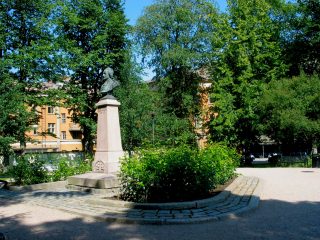 Chydeniuksen puisto kesäisenä päivänä. Anders Chydeniuksen patsaaseen loistaa aurinko.